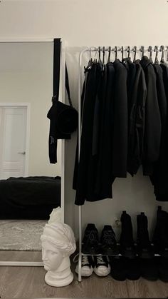 a white mannequin head sitting next to a closet filled with black shirts and shoes