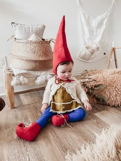 a small child sitting on the floor wearing a red and blue gnome's hat