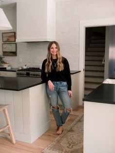 a woman standing in a kitchen next to a counter top and sink with an island