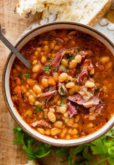 a bowl of beans and ham soup with bread on the side