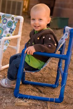 a little boy sitting on top of a blue chair in the dirt next to a fence