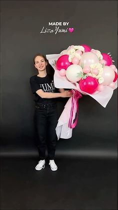 a woman holding a bouquet of balloons in front of a black wall with the words made by lise yumin written on it