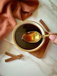 a spoon full of liquid sitting on top of a white table next to cinnamon sticks