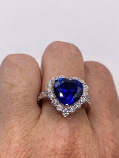 a woman's hand holding a blue and white heart shaped ring with diamonds around it