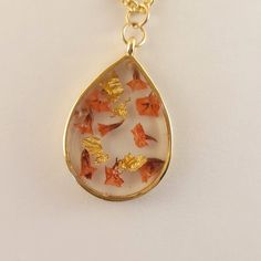 a gold plated necklace with orange flowers in the shape of a tear on a white background