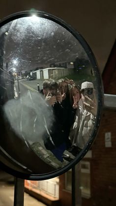 the reflection of two people in a round mirror on a metal pole outside at night