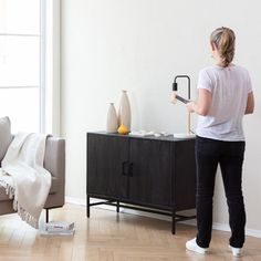 a woman standing in front of a couch holding a paint roller and painting the wall