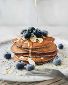 a stack of pancakes with blueberries and almonds being drizzled with syrup