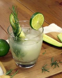 an alcoholic drink is garnished with rosemary and limes on a cutting board