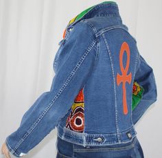 Handcrafted One-Of-A-Kind Upcycled jean jacket Elevate your wardrobe with our Afrocentric jean jacket. Upcycled from thrifted denim, this one-of-a-kind plus size jacket embodies Afro-modern fashion and African heritage. The centerpiece of this jacket is an orange genuine leather Ankh appliqué. The Ankh, an ancient Egyptian hieroglyphic symbol representing "life," adds depth and meaning to the jacket's design. Bold orange vinyl text on one sleeve spells out 'Life', resonating with the wearer's sp Fitted Denim Jacket In Recycled Denim, Fitted Recycled Denim Jacket, Blue Fitted Recycled Denim Outerwear, Fitted Long Sleeve Denim Jacket In Recycled Denim, Fitted Patchwork Denim Jacket In Recycled Denim, Fitted Patchwork Denim Jacket For Streetwear, Upcycle Jean Jacket, Thrifted Denim, The Ankh