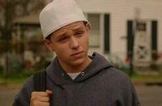 a young man wearing a white hat and holding a black bag in front of a house