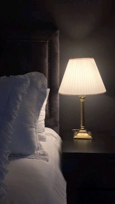 a bed with white pillows and a lamp on top of the night stand next to it