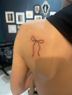 the back of a woman's shoulder with a small bow tattoo on her left side