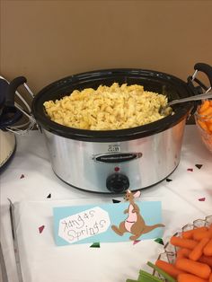 a table topped with a crock pot filled with macaroni and cheese next to carrots