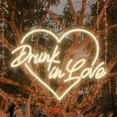 a heart shaped neon sign that reads drunk in love on the side of a tree