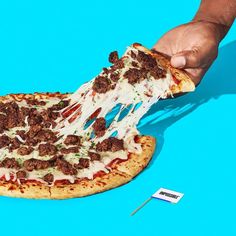 a hand holding a slice of pizza with meat toppings on it and a blue background