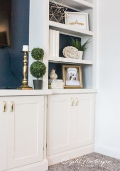 a white bookcase with blue walls and gold accents in a living room area that has carpeted flooring