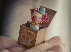 a small toy clown in a wooden box on someone's hand with it's eyes closed