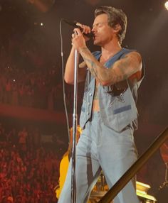 a man with tattoos on his arm holding a microphone while standing in front of a crowd