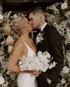 a bride and groom kissing in front of a floral arch with white flowers on it