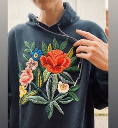 a person wearing a hoodie with flowers on it holding something in one hand and pointing to the other