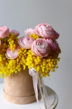 pink and yellow flowers in a vase with a ribbon on the top, sitting on a white table