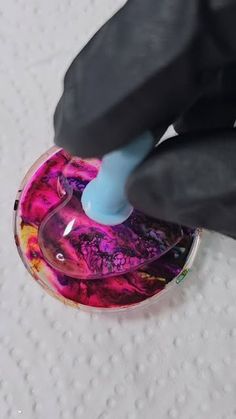 a person with black gloves is using a blue plastic object to paint the inside of a glass bowl