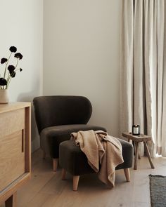 a chair with a blanket on it next to a table and flowers in a vase