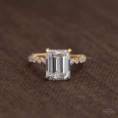 an emerald - cut diamond ring is displayed on a brown surface with diamonds around it