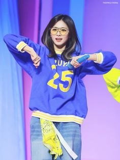 a woman wearing glasses and a blue sweatshirt is standing on stage with her hands in the air