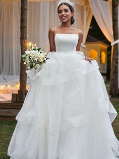 a woman in a white wedding dress standing on the grass with her hand on her hip