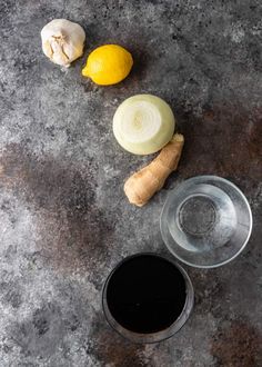 an overhead view of some vegetables and a glass of black liquid on a gray surface