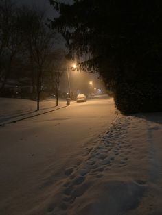 a snowy street at night with cars parked on the side and trees in the background