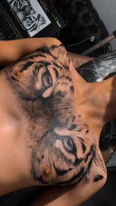 a man with a tiger tattoo on his chest laying in front of a laptop computer