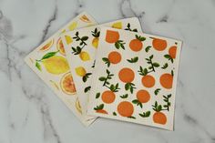 three napkins with oranges on them sitting on a marble counter top next to each other