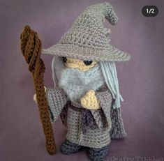 a crocheted wizard doll holding a wand and wearing a gray hat with grey hair