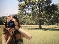 a woman taking a photo with her camera in front of a tree and grass field