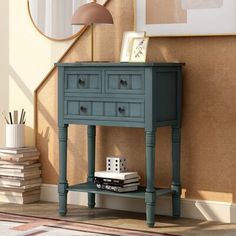 a small blue table with drawers in front of a mirror and books on the floor