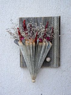 an old fan with dried flowers on it mounted to the side of a white wall