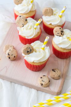 cupcakes with white frosting and chocolate chip cookies on a wooden cutting board