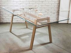 a glass table with wooden legs in front of a white brick wall and flooring