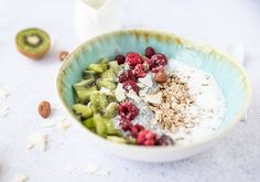 a bowl filled with granola, raspberries, kiwis and nuts