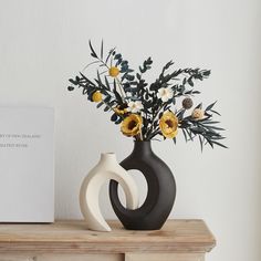 a black and white vase with yellow flowers on a wooden table next to a card