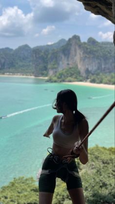 a woman climbing up the side of a cliff with a rope in front of her