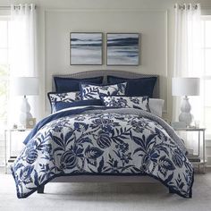 a bed with blue and white comforters in a bedroom next to two windows,