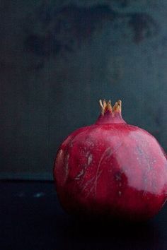 a red pomegranate sitting on top of a black table next to a gray wall