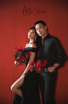 two people standing next to each other in front of a red wall with flowers on it