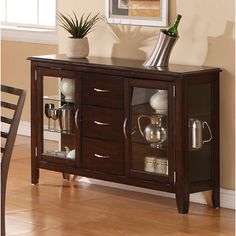 a wooden sideboard with glass doors and two vases on the top, in front of a dining room table