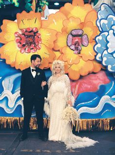 a man and woman standing next to each other in front of a large flower wall