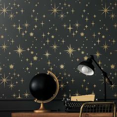 a desk with a typewriter, lamp and stars wallpaper on the wall behind it